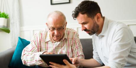 Älterer und jüngerer Mann schauen auf ein Tablet